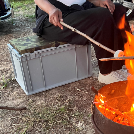 Person sitzt auf einer Seat Box am Lagerfeuer