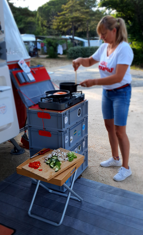 Eine Frau kocht auf einem Campingkocher, der auf Euroboxen steht.