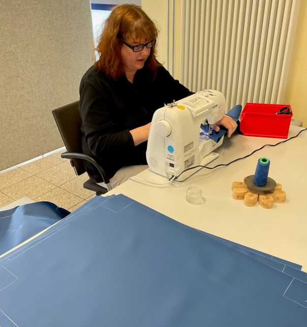 Frau f&uuml;hrt N&auml;harbeiten an blauem Stoff an einer N&auml;hmaschine durch.